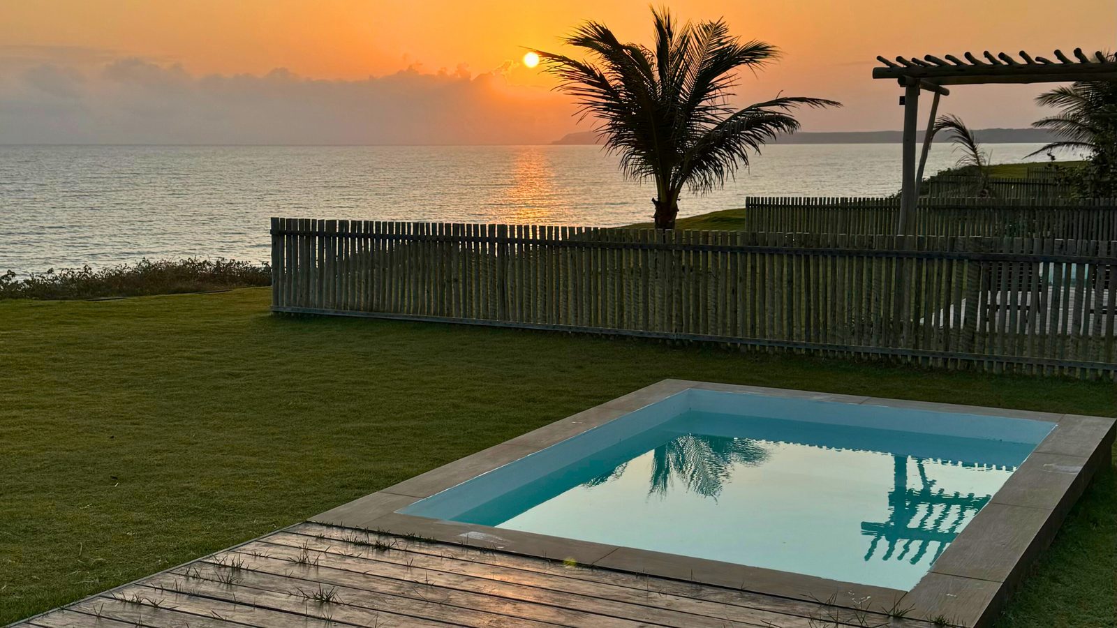 Piscina no gramado com pergolado e vista para o mar